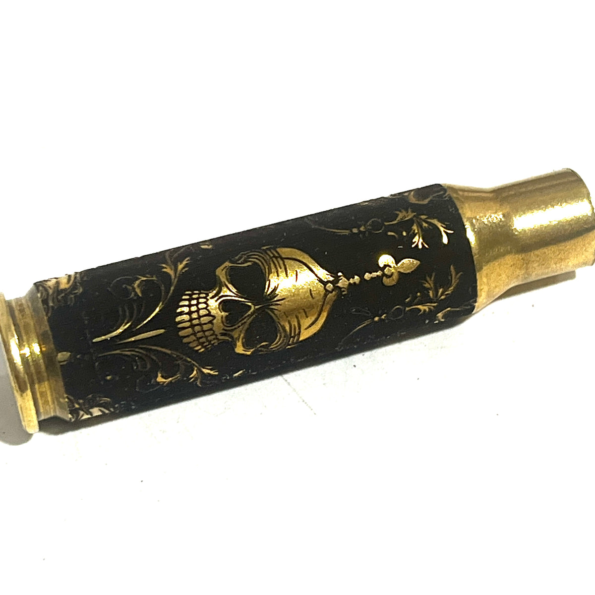 Brass rifle casing engraved with a gold gothic skull wearing a crown and scrollwork design on a black background