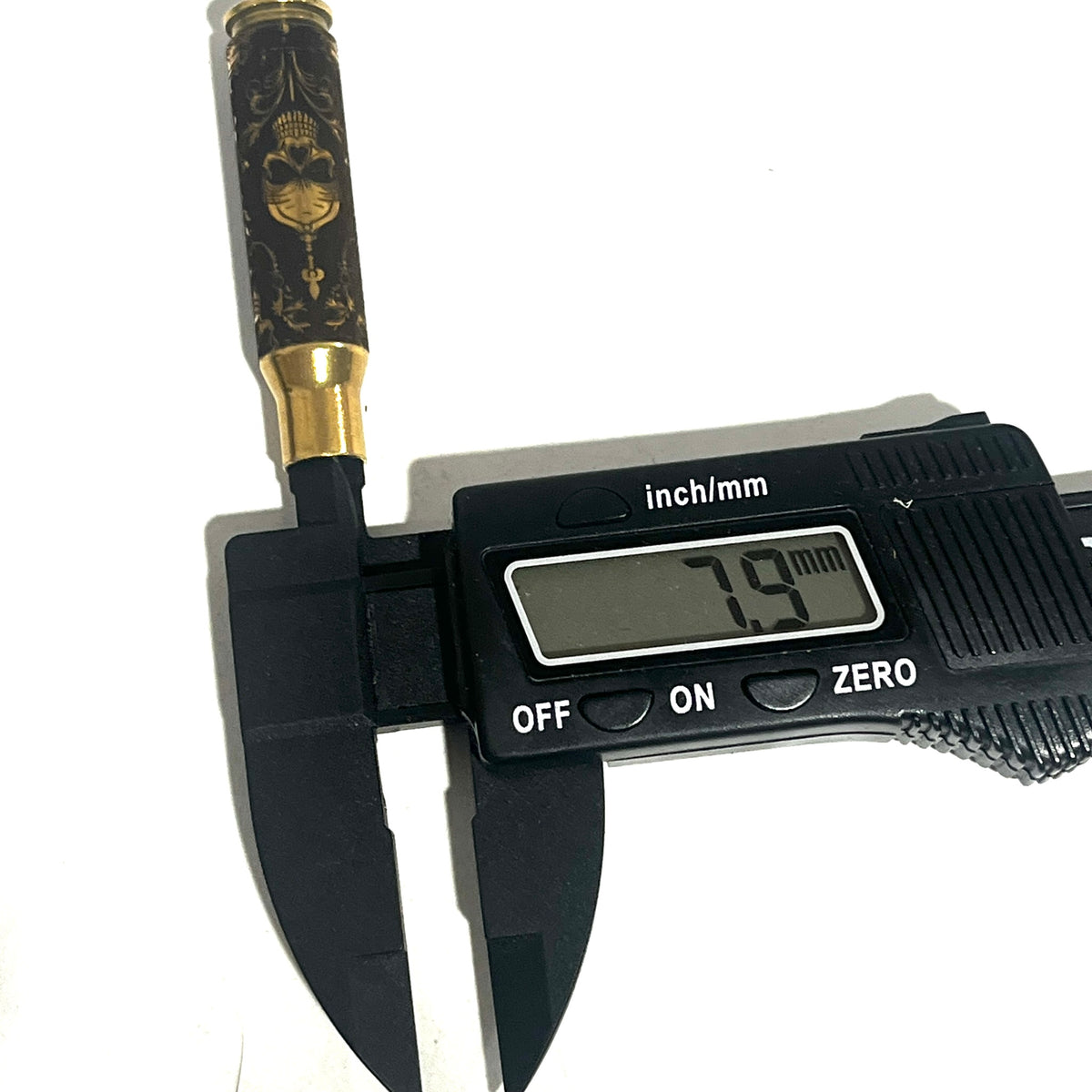 Digital caliper measuring the diameter of a brass rifle casing engraved with a gothic skull design at 7.9 mm