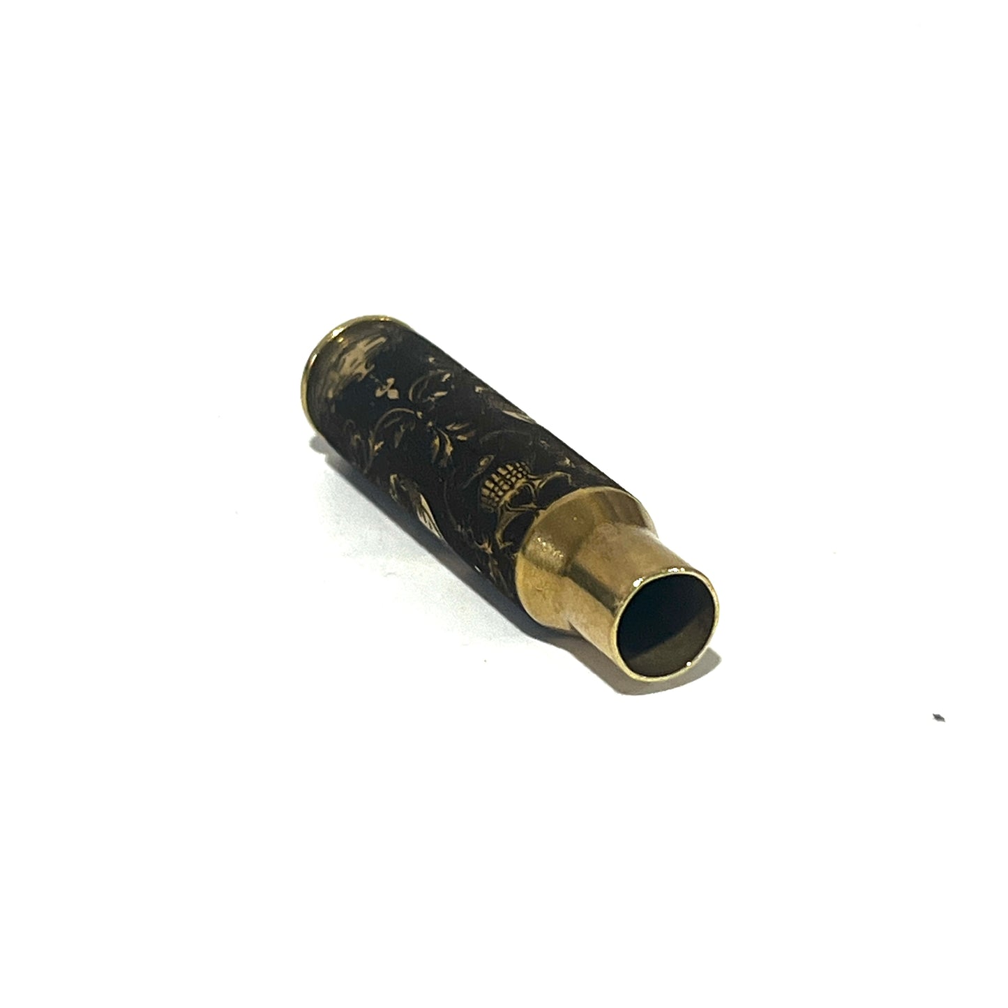 Brass rifle casing engraved with a gold gothic skull and floral scrollwork design, laid diagonally on white background