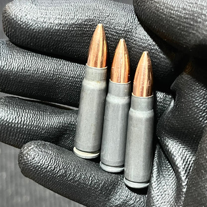 Three gray steel AK47 casings with copper bullets held upright in a black gloved hand.