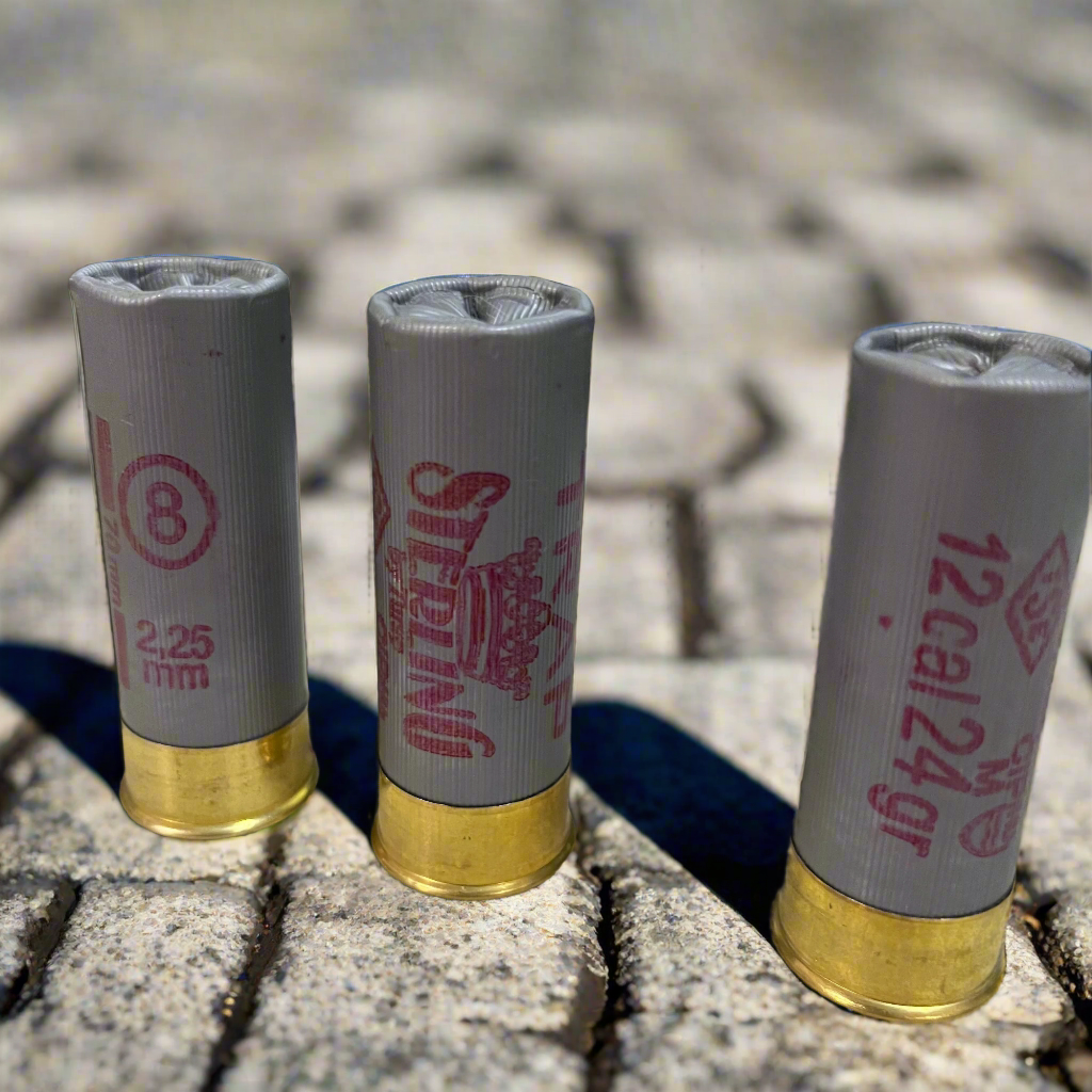 3 gray Sterling 12 gauge shotgun shells standing on a brick surface with pink stamped text