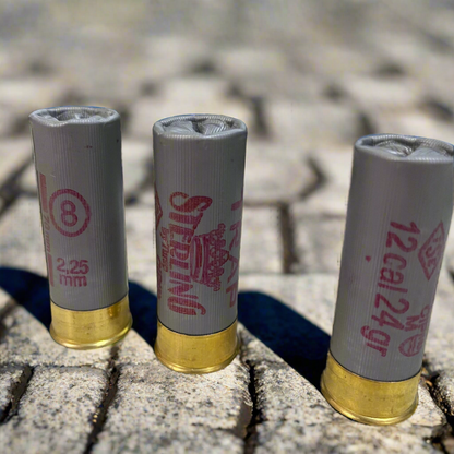 3 gray Sterling 12 gauge shotgun shells standing on a brick surface with pink stamped text