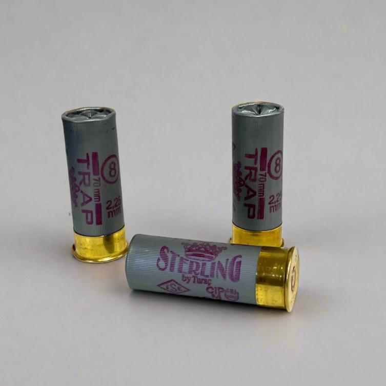 3 gray Sterling Trap 8 shot 2.25 mm 12 gauge shotgun shells, 2 standing and 1 lying down on a gray background