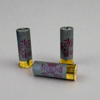 3 gray Sterling Trap 8 shot 2.25 mm 12 gauge shotgun shells, 2 standing and 1 lying down on a gray background