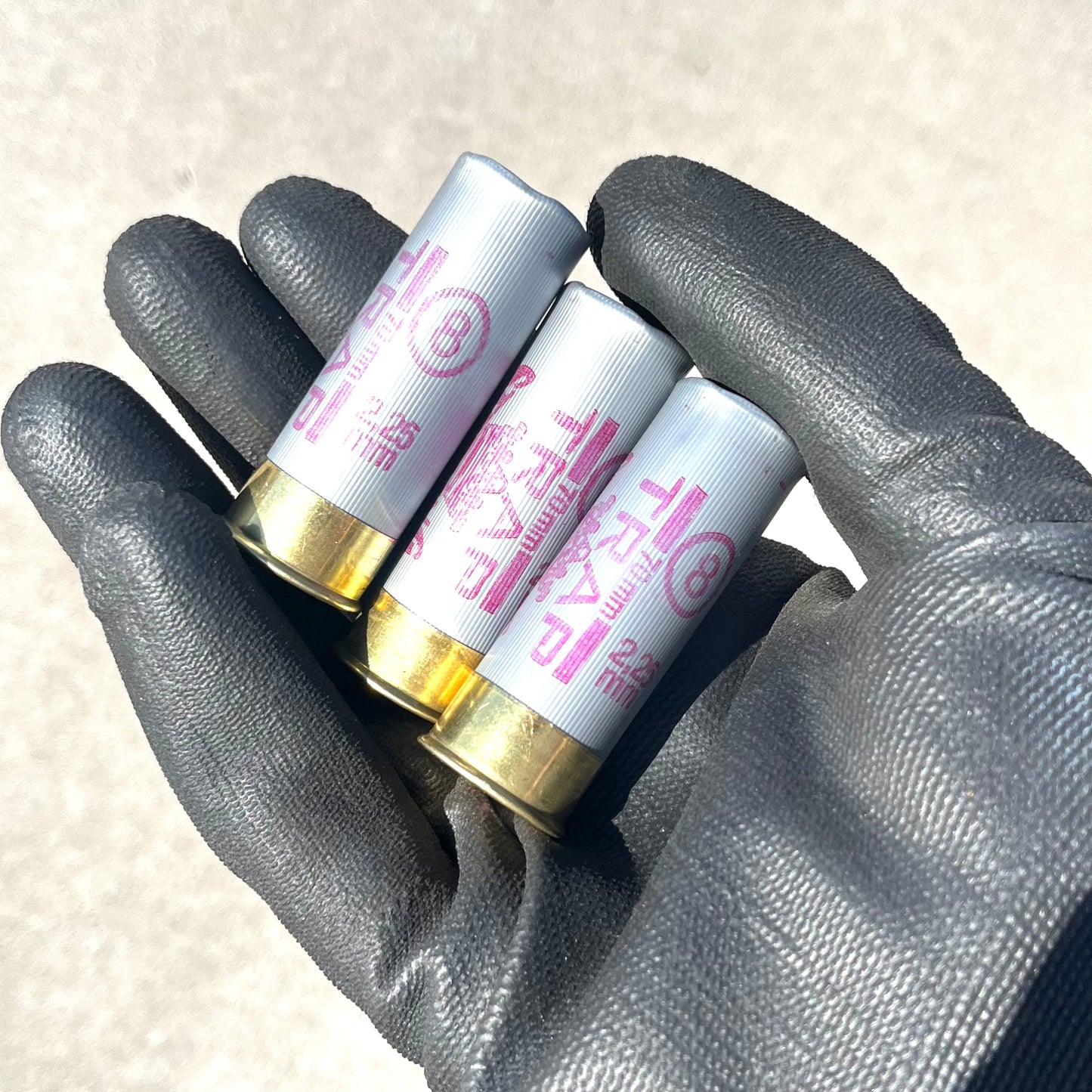 A gloved hand holding 3 gray Sterling Trap 12 gauge shotgun shells with brass bases