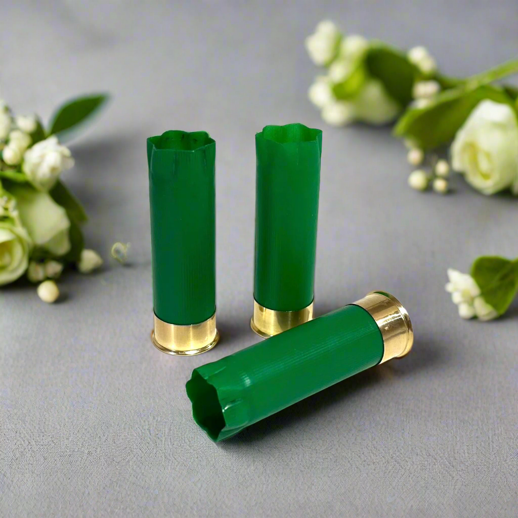 3 empty green 12 gauge shotgun shells with crimped open ends and brass bases displayed on a gray surface with white flowers