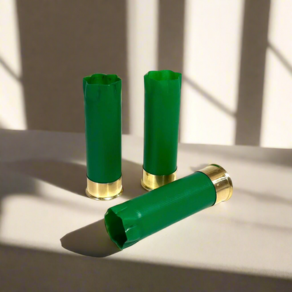 3 empty green 12 gauge shotgun shells with crimped open ends and brass bases on a sunlit surface