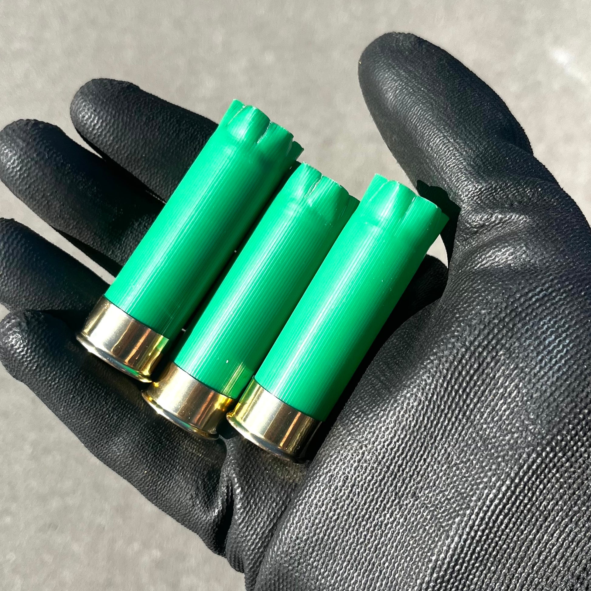 3 empty green 12 gauge shotgun shells held in a gloved hand