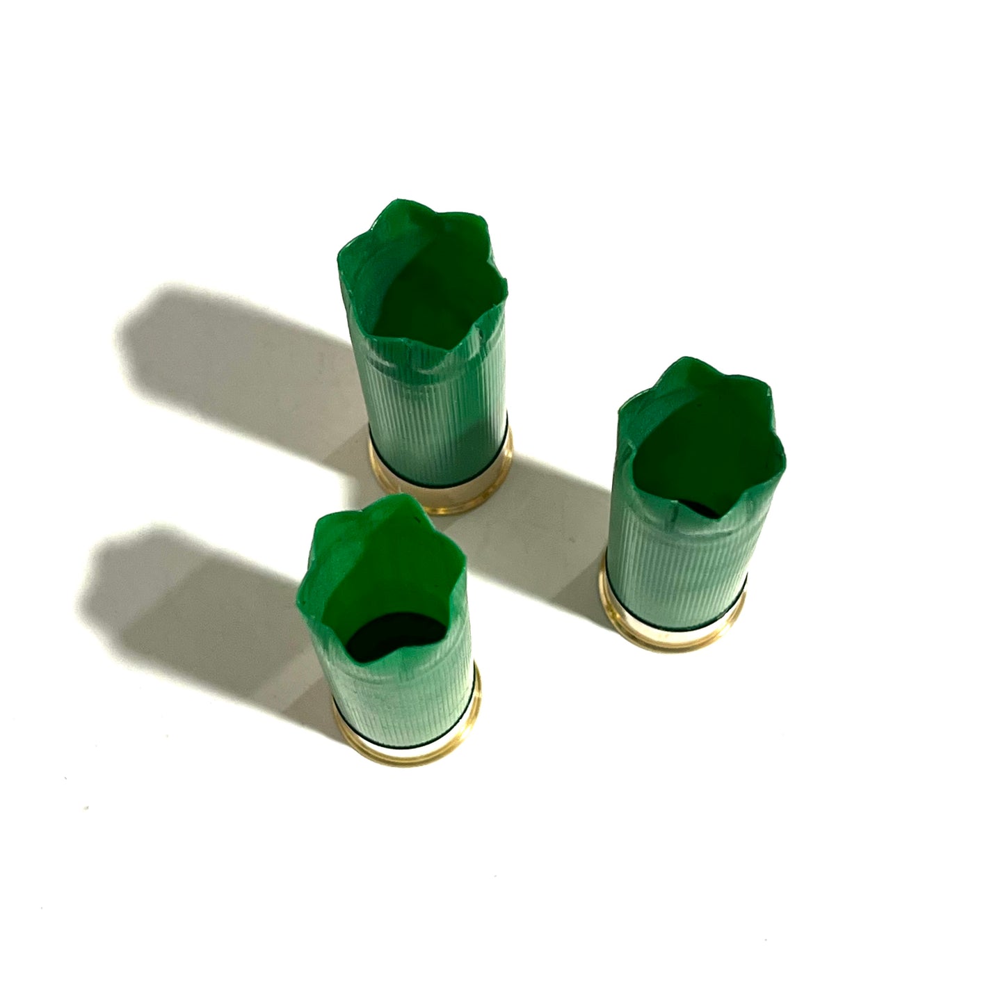 3 empty green 12 gauge shotgun shells with open crimped ends viewed from above showing hollow interior
