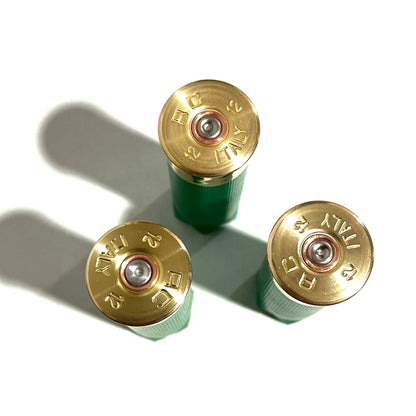 3 empty green 12 gauge shotgun shells viewed from above showing brass headstamps marked RC 12 Italy