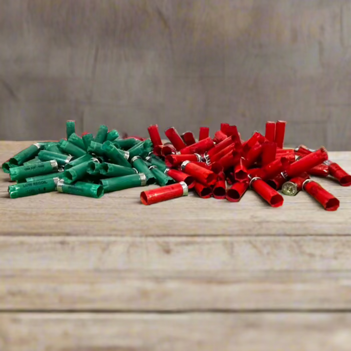 2 piles of empty shotgun shells, one green and one red, side by side on a wood plank surface