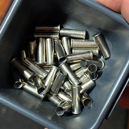 A hand holding a black tray full of loose nickel 22 caliber empty casings