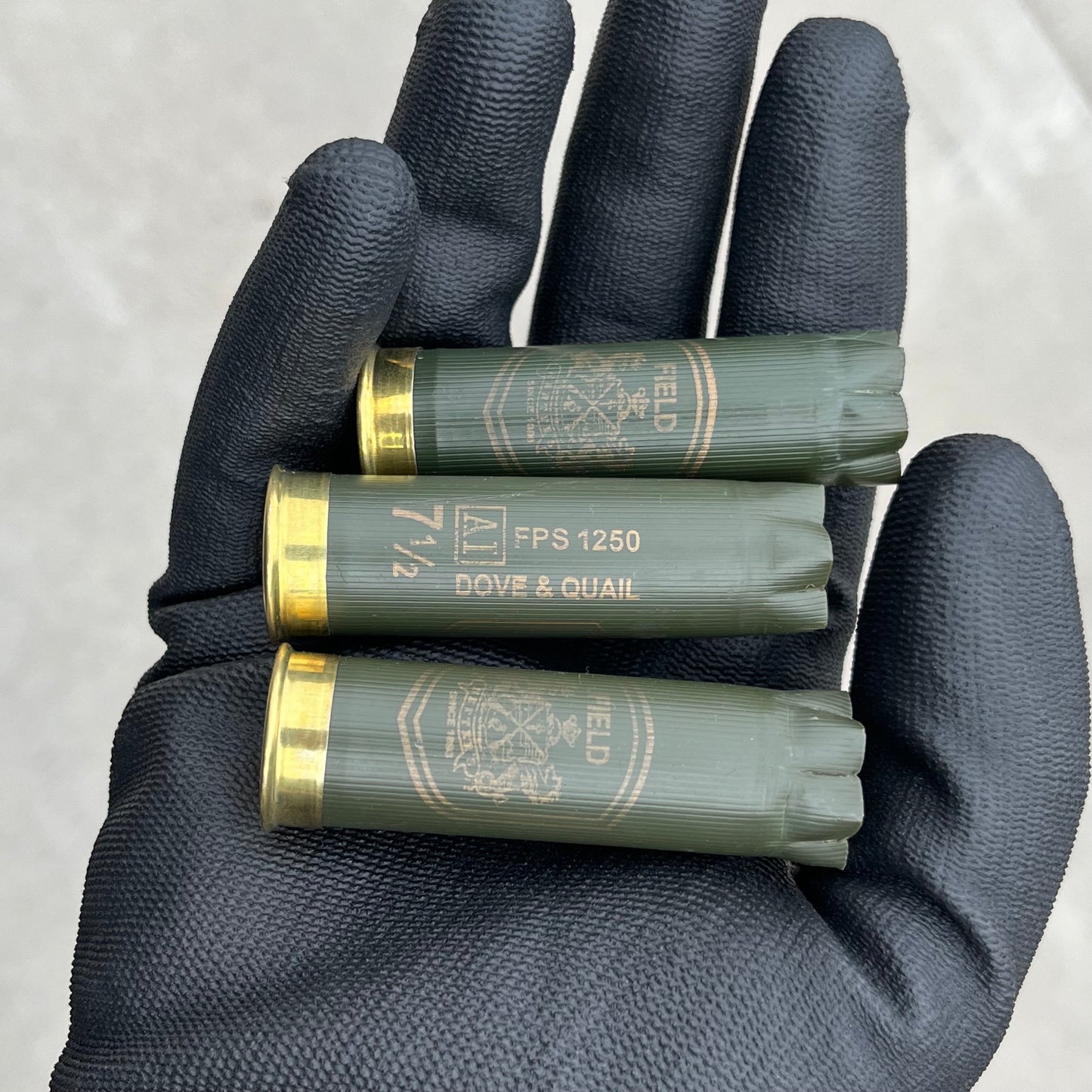 3 empty herters 12 gauge green hulls in black gloved hand showing brass headstamps