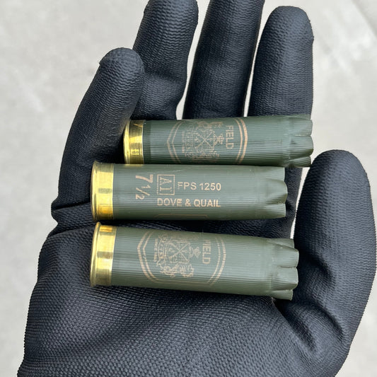 3 empty herters 12 gauge green hulls in black gloved hand showing brass headstamps