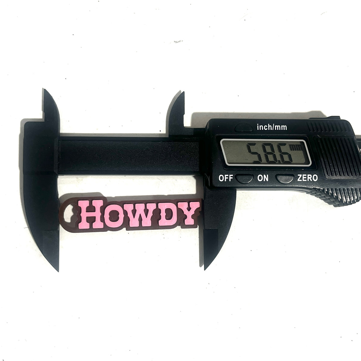 Digital caliper measuring the length of a pink and brown HOWDY charm at 58.6mm