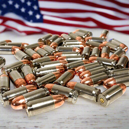 A pile of nickel 45 ACP pistol cartridges with copper bullets in front of a blurred American flag.