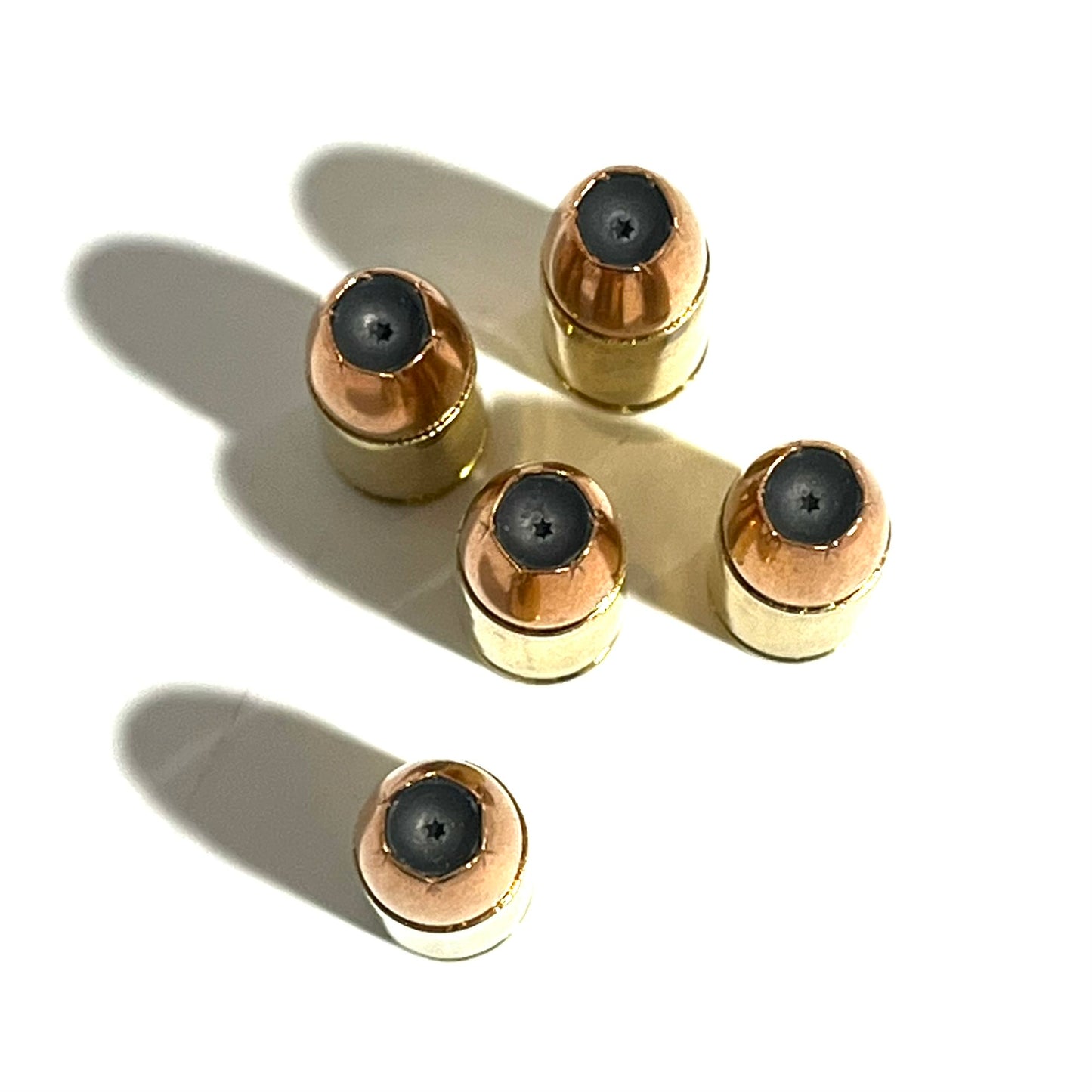 Five inert 9mm hollow point shells arranged on white with dark jacketed bullet tips facing upward towards camera.