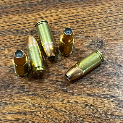 Inert 9mm JHP dummy rounds resting at varied angles on a wooden surface showing brass bodies and copper bullet tips.