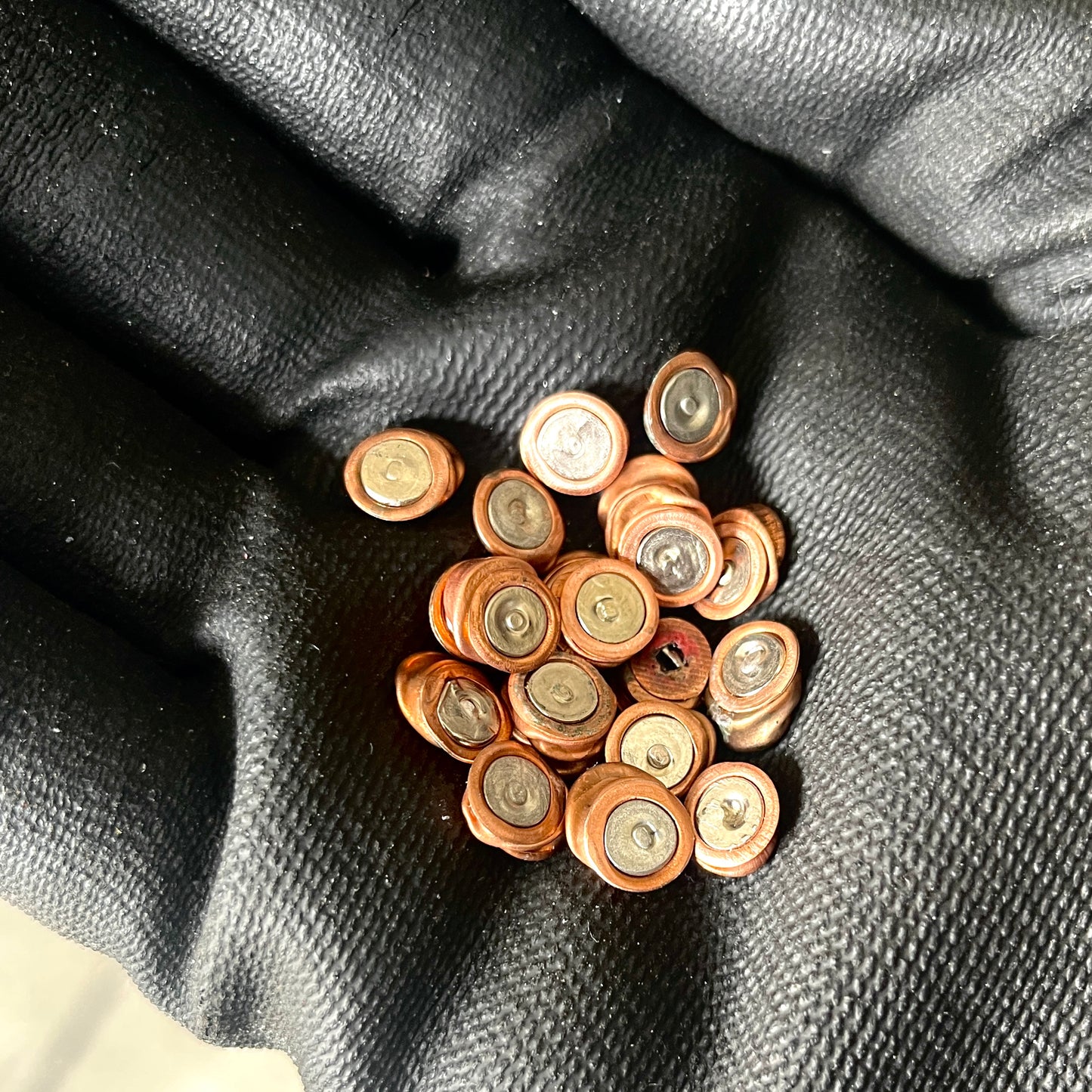 A cluster of mixed copper and silver inert primer discs held in a gloved hand, showing flattened details.