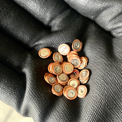 A cluster of mixed copper and silver inert primer discs held in a gloved hand, showing flattened details.