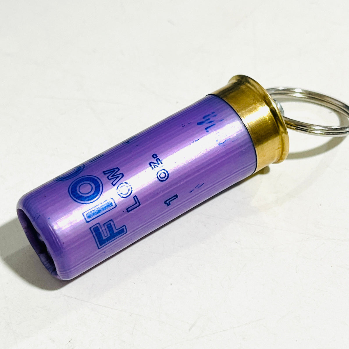 Lavender Fiocchi Low Recoil 12 gauge once-fired hull keychain lying on its side with brass head and split ring