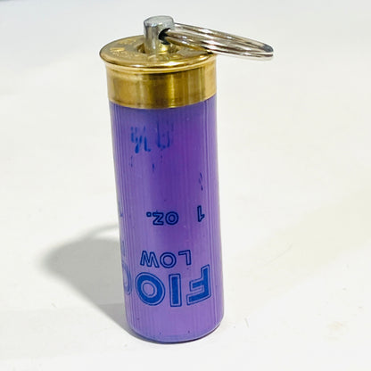 Spent lavender Fiocchi hull keychain standing upright on its crimp end, brass head and split ring on top