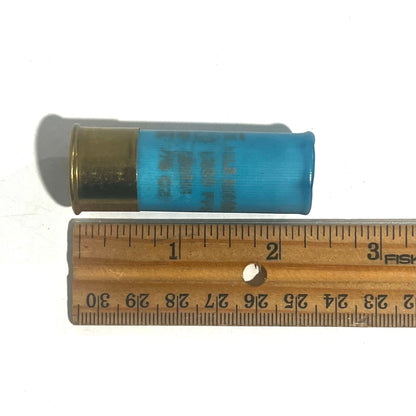 Single light blue 12 gauge shotgun shell hull with a high brass base shown beside a wooden ruler for scale