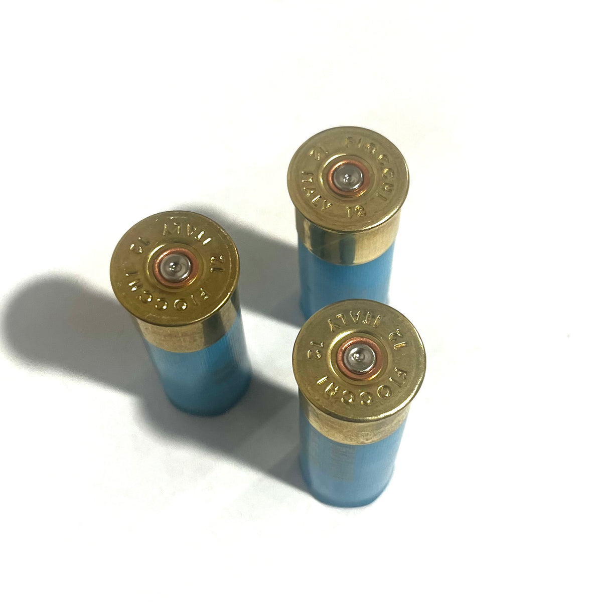 Three light blue 12 gauge shotgun shell hulls showing brass "FIOCCHI 12 ITALY" headstamps with spent primers