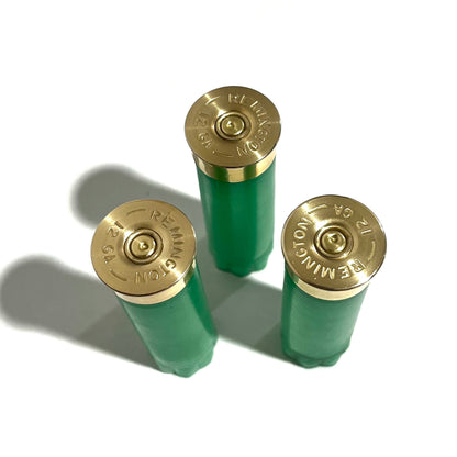 3 gold 12 gauge shotgun shell base caps stamped Remington 12GA on light green hulls, viewed from above