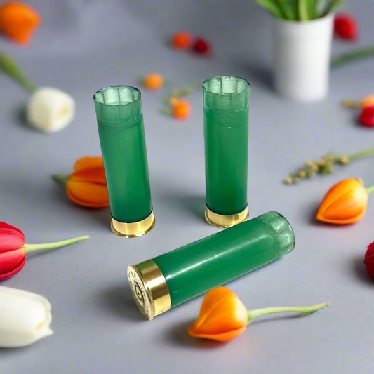 3 light green 12 gauge shotgun shell hulls with gold bases on a gray surface surrounded by orange and white flowers