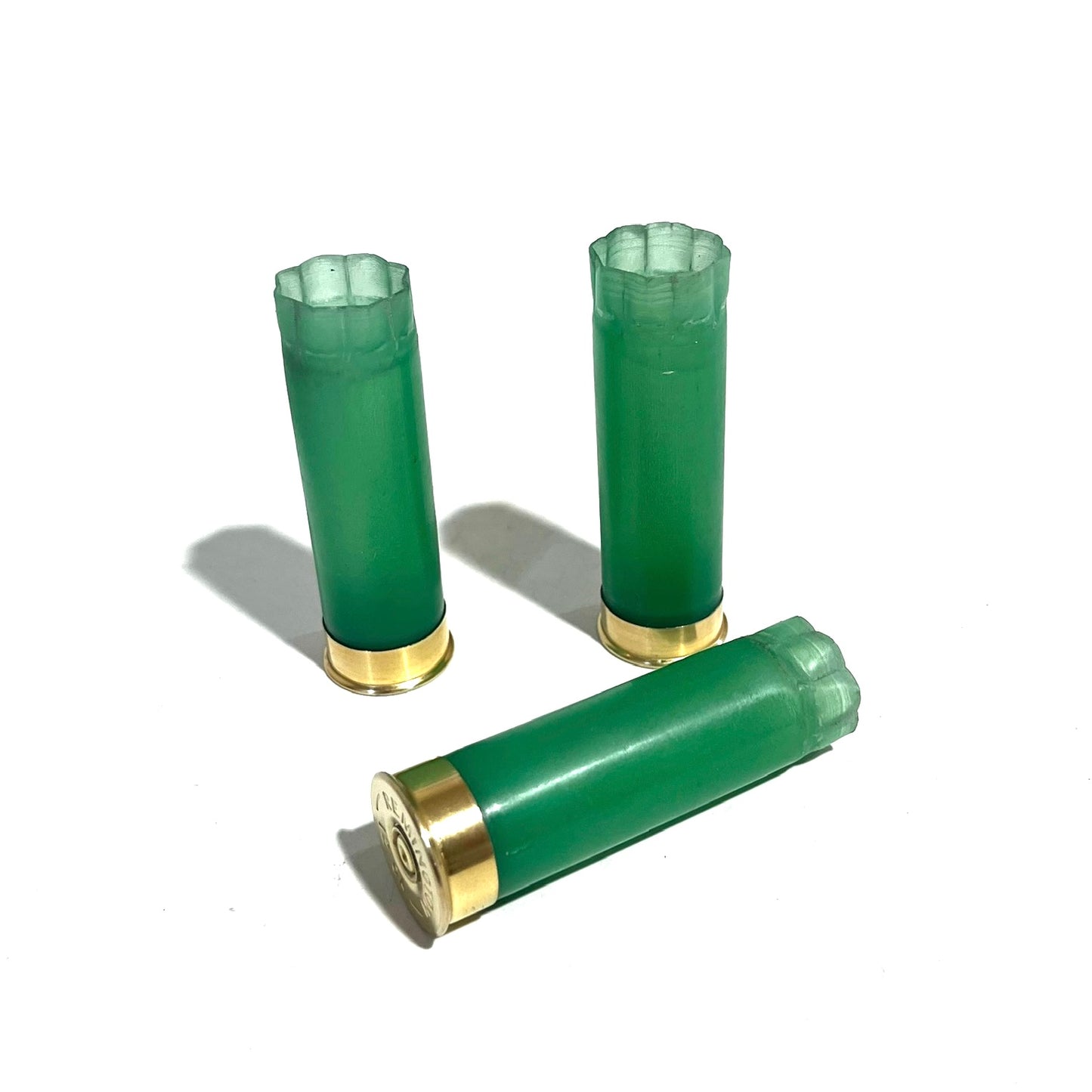 3 light green 12 gauge shotgun shell hulls with gold bases, two standing and one lying, on a white background