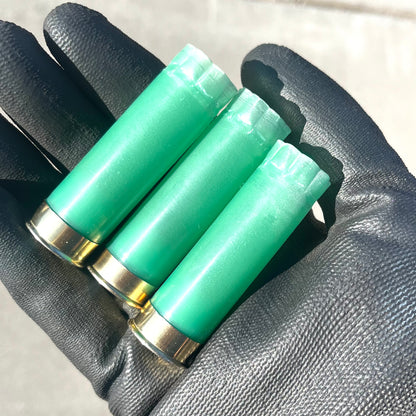 3 light green 12 gauge shotgun shell hulls with gold bases held in a gloved hand