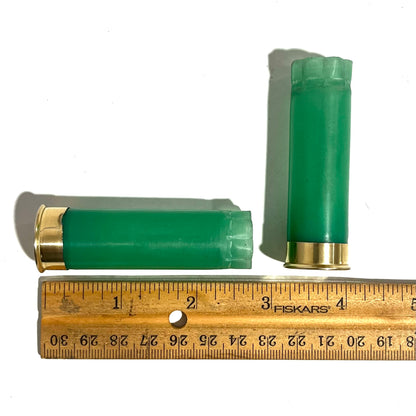 2 light green 12 gauge shotgun shell hulls measured on a wood ruler, one standing and one lying, approximately 2.75 inches