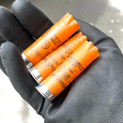 Gloved hand holding three light orange 12 gauge empty shotgun shells printed with Target Recoil and Nobelsport Italia markings