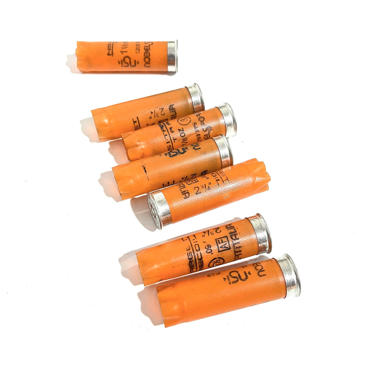 Seven light orange 12 gauge empty shotgun shells with silver bases lying on their sides on a white background