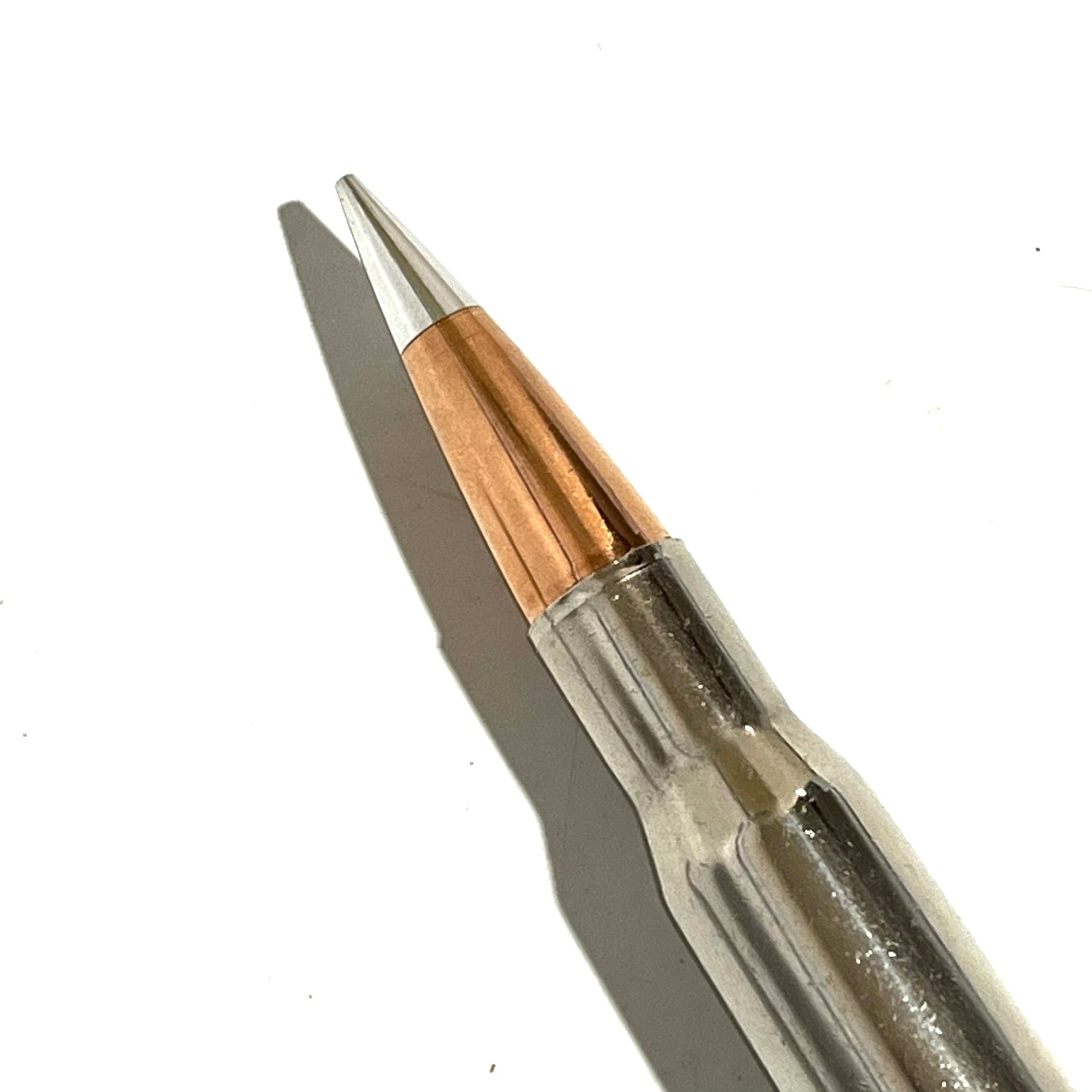 Macro shot of sharp copper Hornady A-Max bullet tip seated in polished silver nickel 50 cal BMG dummy casing.
