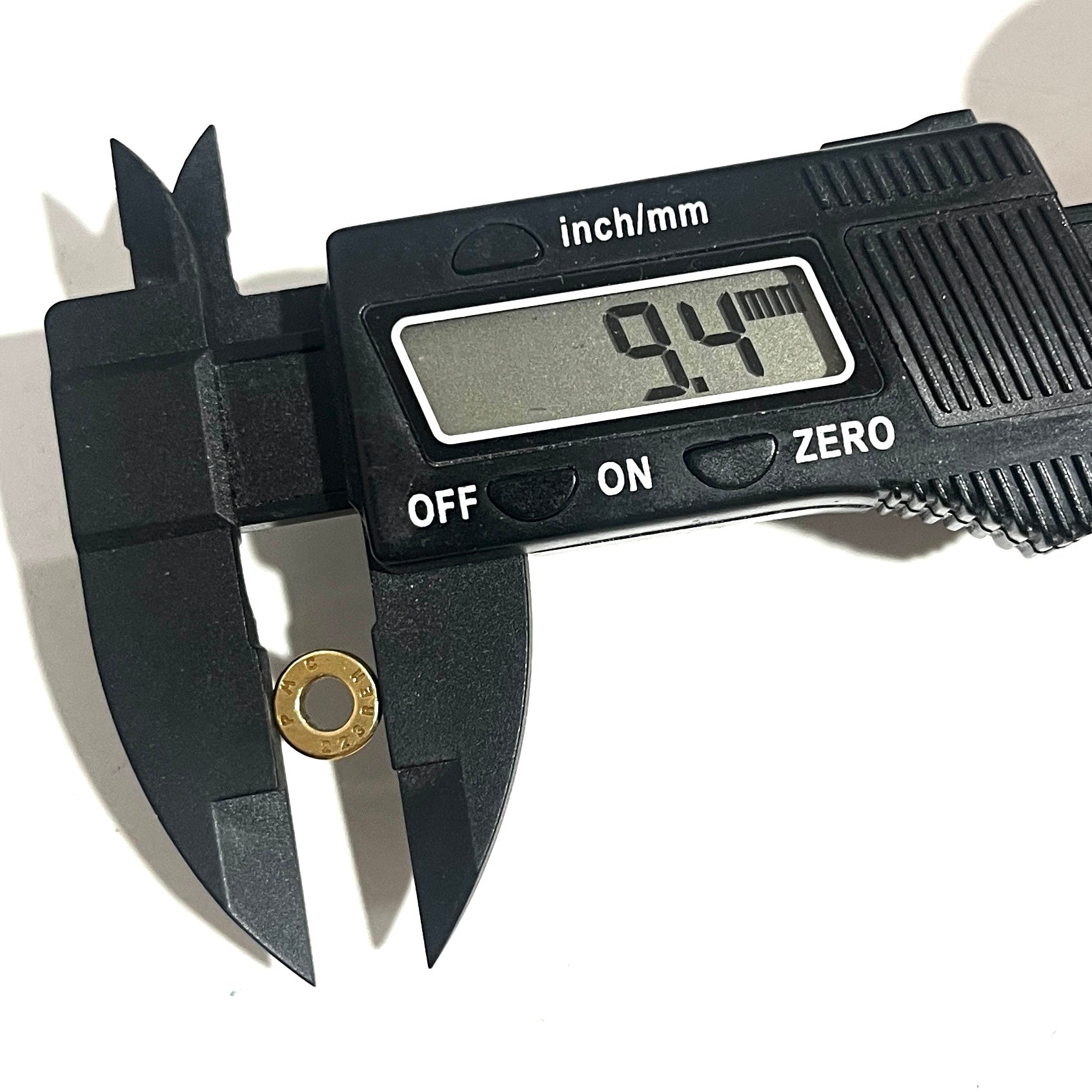 Digital caliper measuring the diameter of a deprimed brass bullet slice showing 9.4 mm