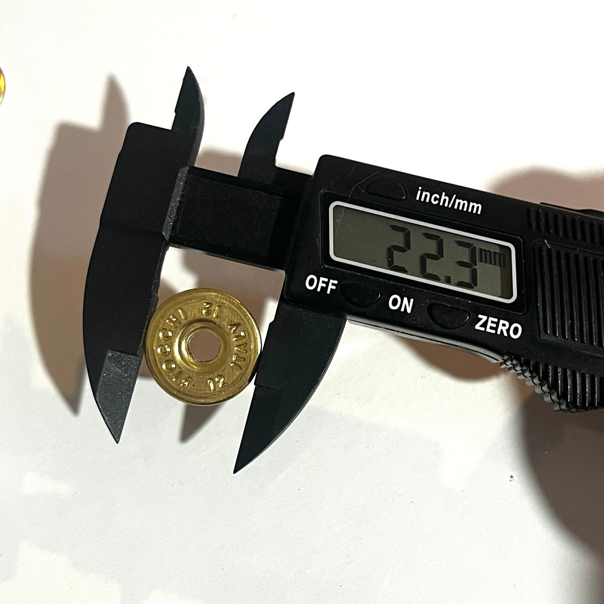 Digital caliper measuring a round brass 12 gauge Fiocchi headstamp slice at 22.3 mm diameter