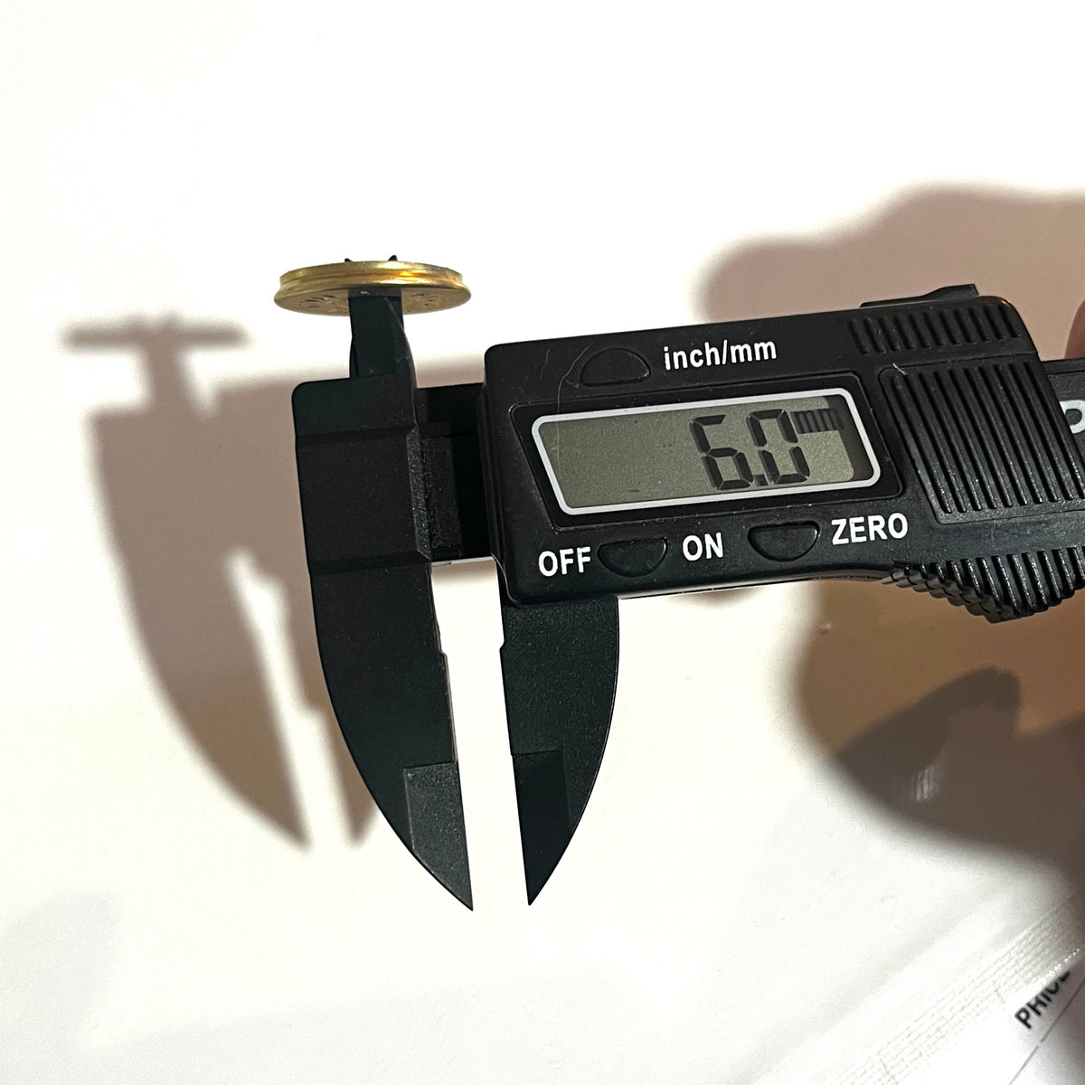 Digital caliper measuring the punched hole diameter of a brass 12 gauge shotgun shell slice at 6.0 mm