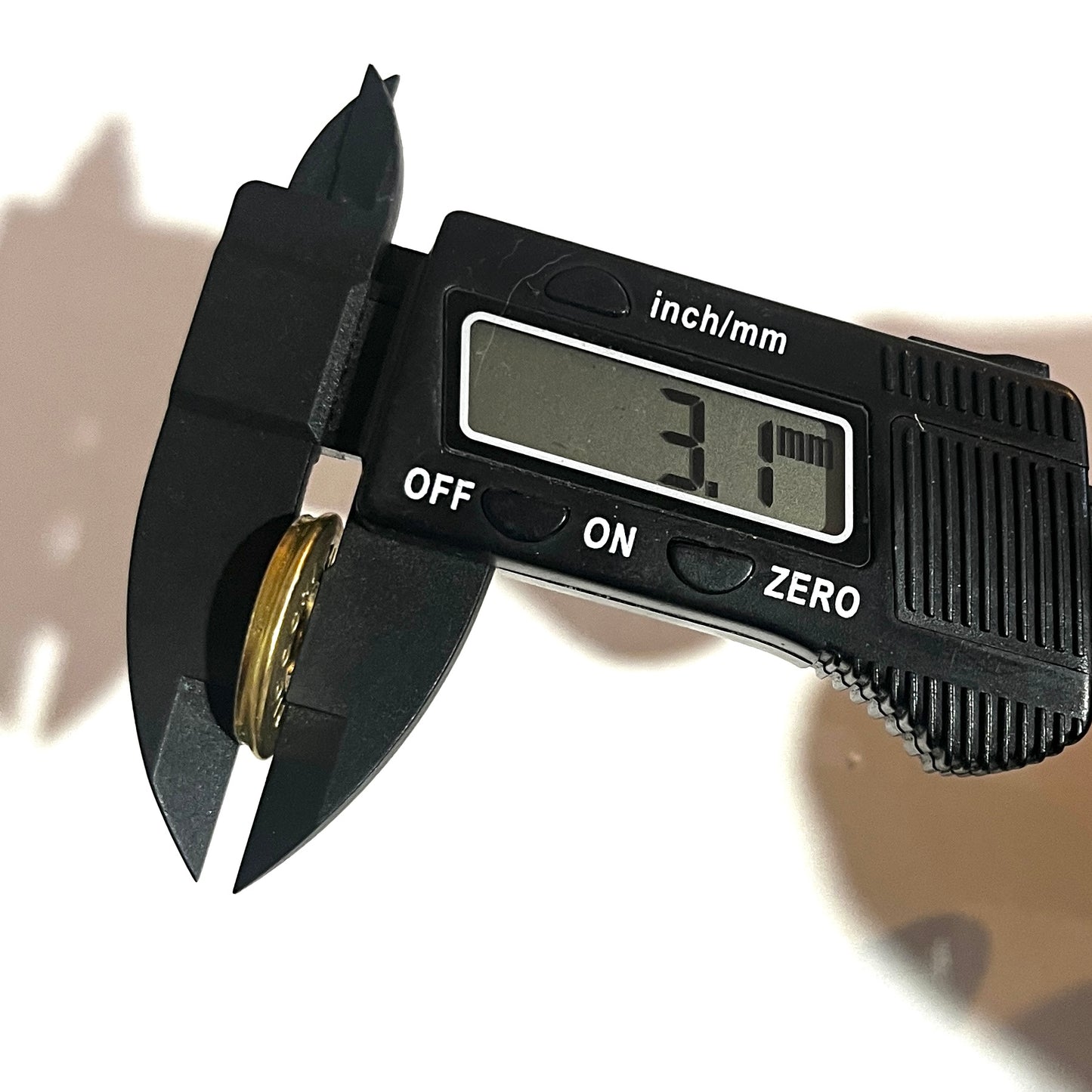 Digital caliper measuring the thickness of a round brass 12 gauge shotgun shell slice at 3.1 mm