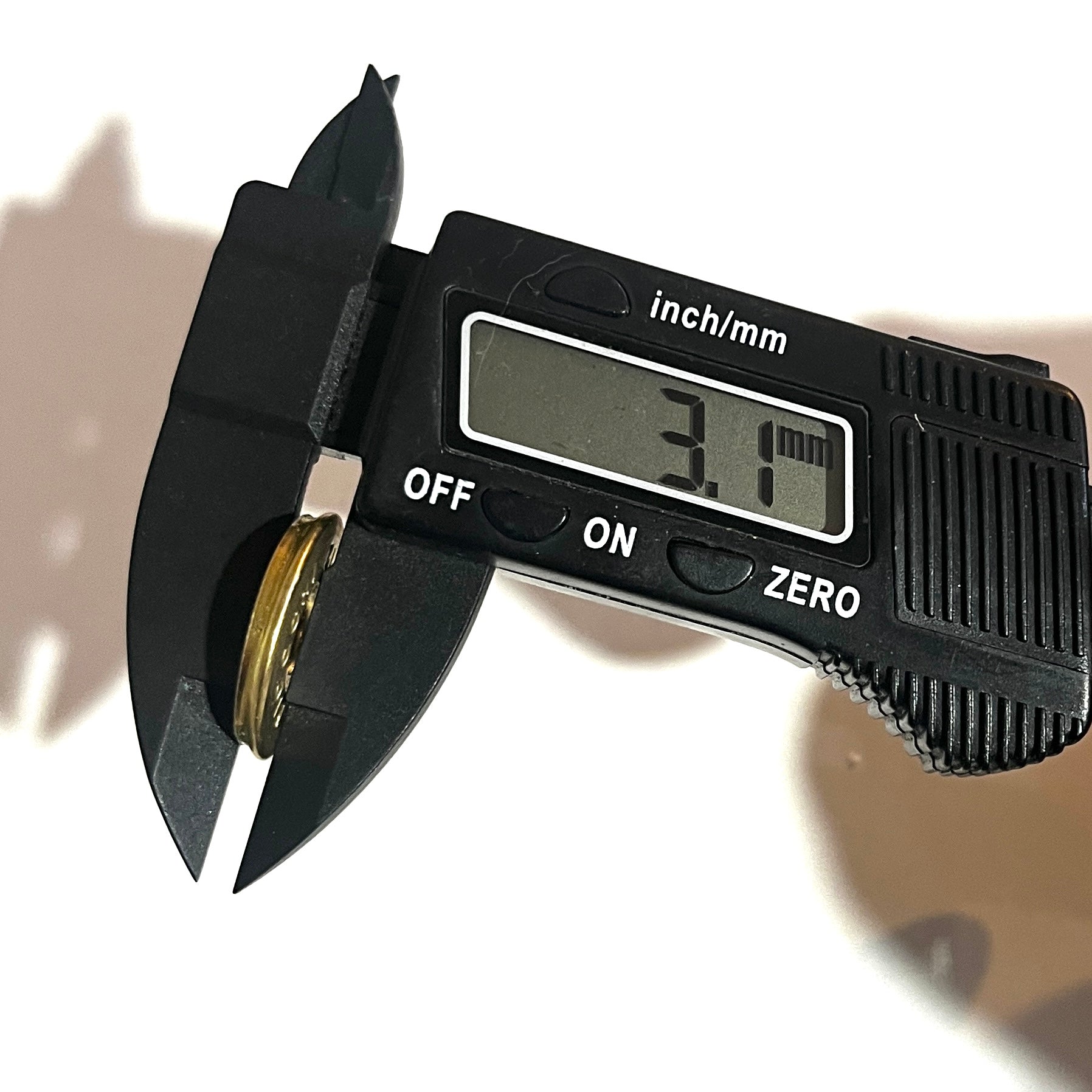 Digital caliper measuring the thickness of a round brass 12 gauge shotgun shell slice at 3.1 mm