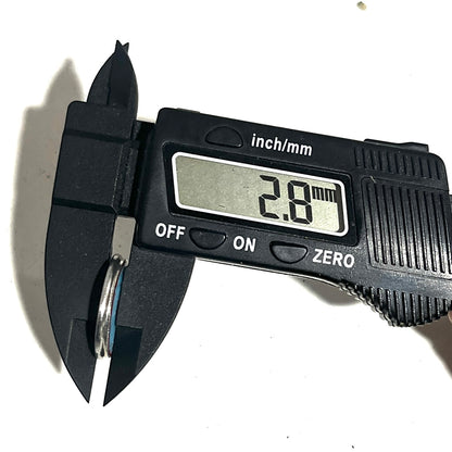 A digital caliper measuring the hole size of a hand painted shotgun shell slice on a white background.
