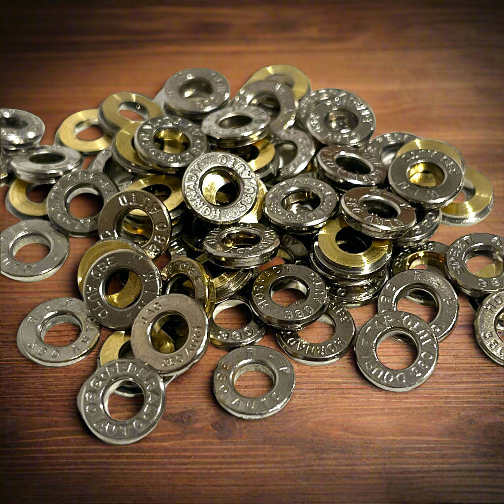 Pile of deprimed silver nickel 380 Auto casing slices on dark wood, showing readable Hornady and WIN headstamps.