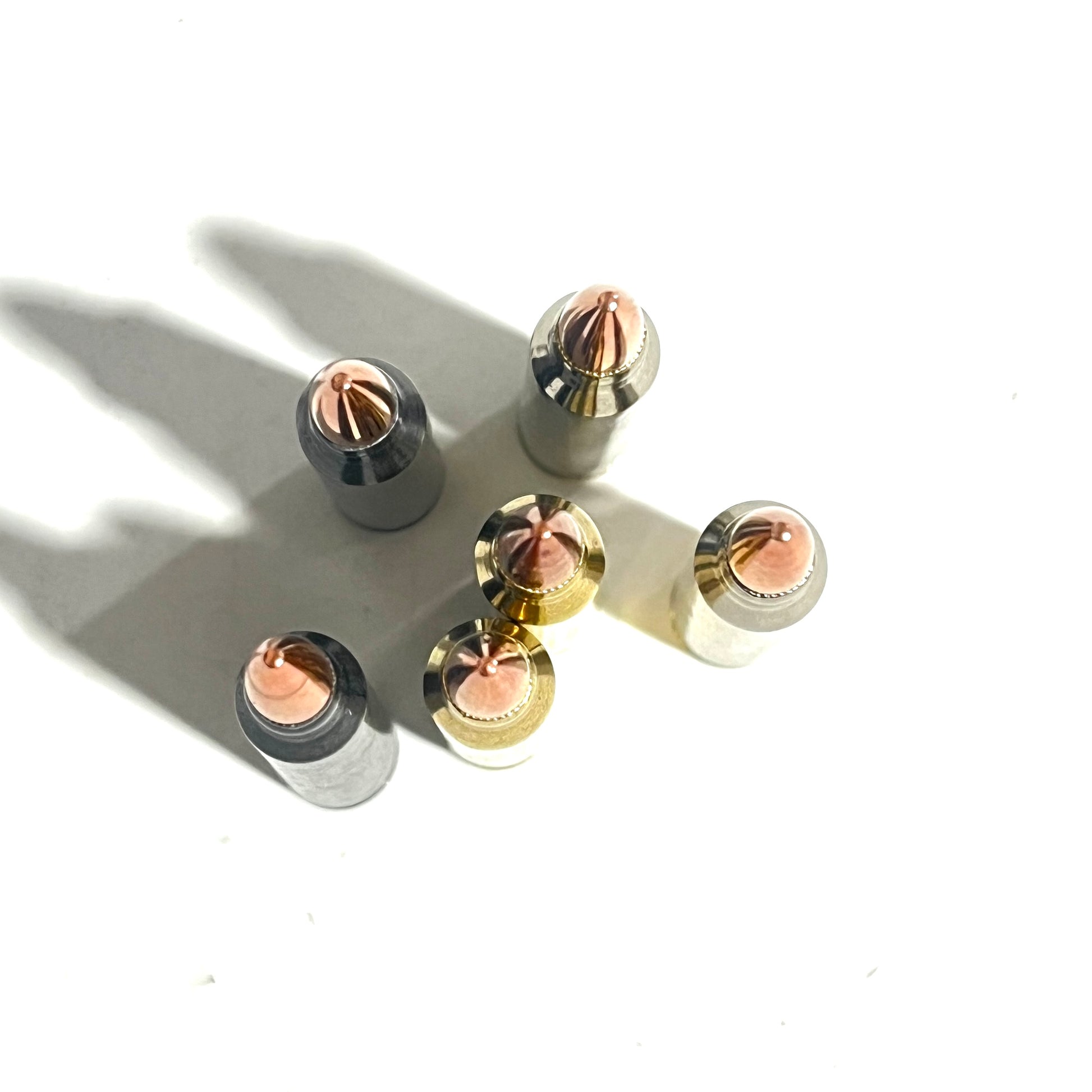 Six .223/5.56 dummy rounds in black, gold, and silver finishes viewed from above, tips clustered together.