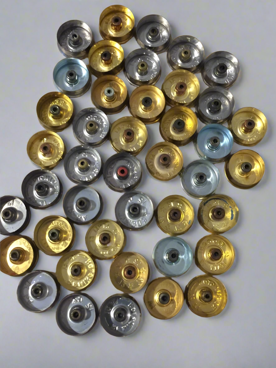 A collection of mixed gold and silver-toned 12 gauge shotgun shell headstamps showing showing openings.

