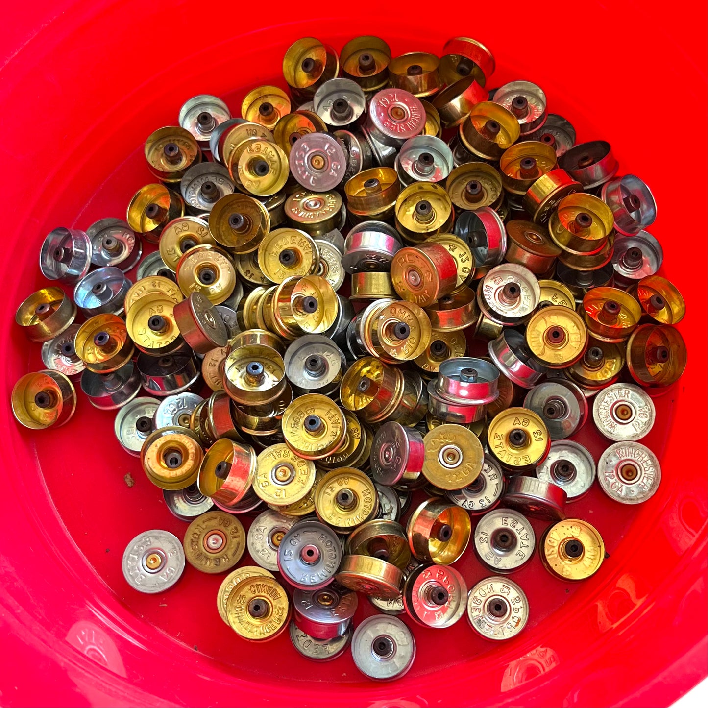 A large collection of mixed gold and silver shotgun shell bases in a bright red container.
