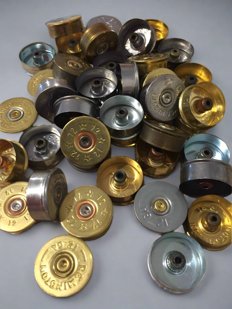 A pile of mixed gold and silver-toned shotgun shell headstamps and metal bases.
