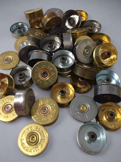 A pile of mixed gold and silver-toned shotgun shell headstamps and metal bases.
