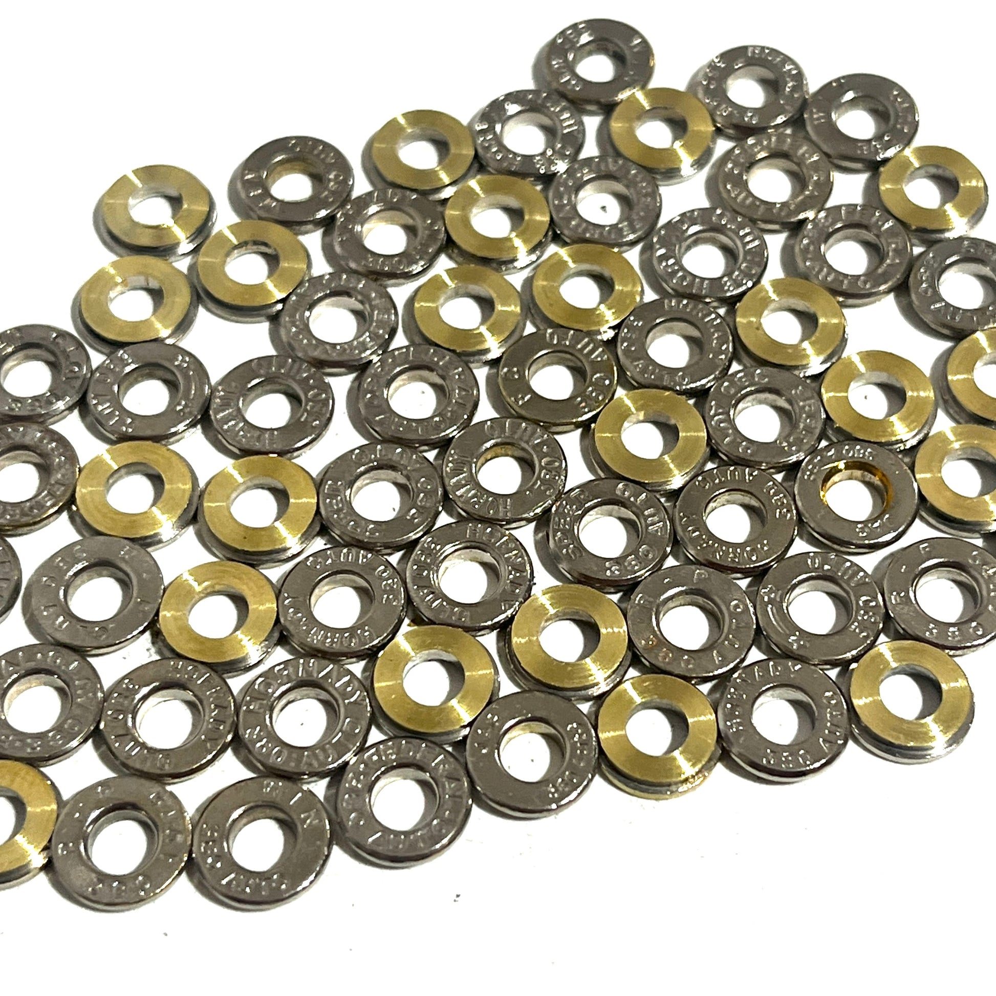 Arrangement of silver nickel and brass 380 Auto bullet slices on white with open deprimed center holes.