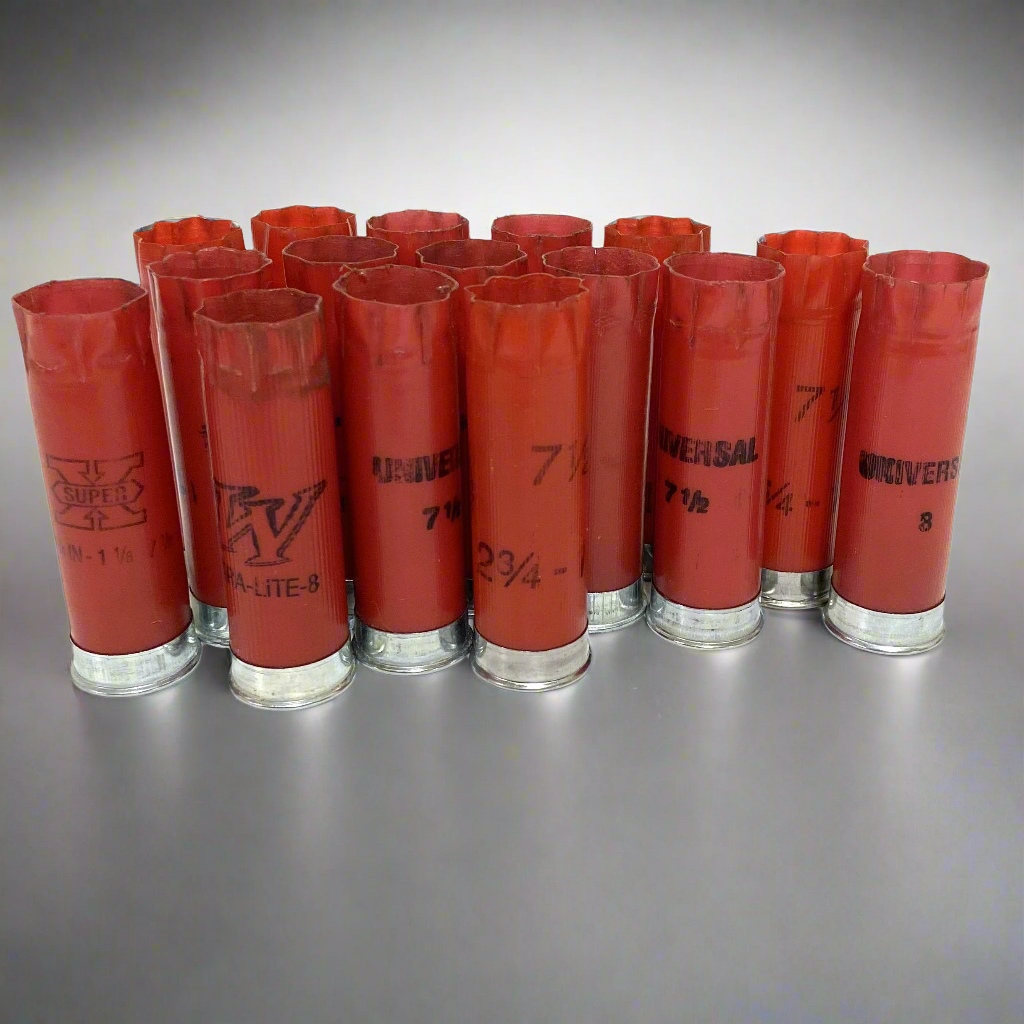 Cluster of recovered, once-fired light red 12-gauge empty shotgun shells standing upright on a grey background. The ribbed plastic hulls feature silver bases, star crimps, and mixed black print showing Winchester "W", "Super X", and "Universal" markings.